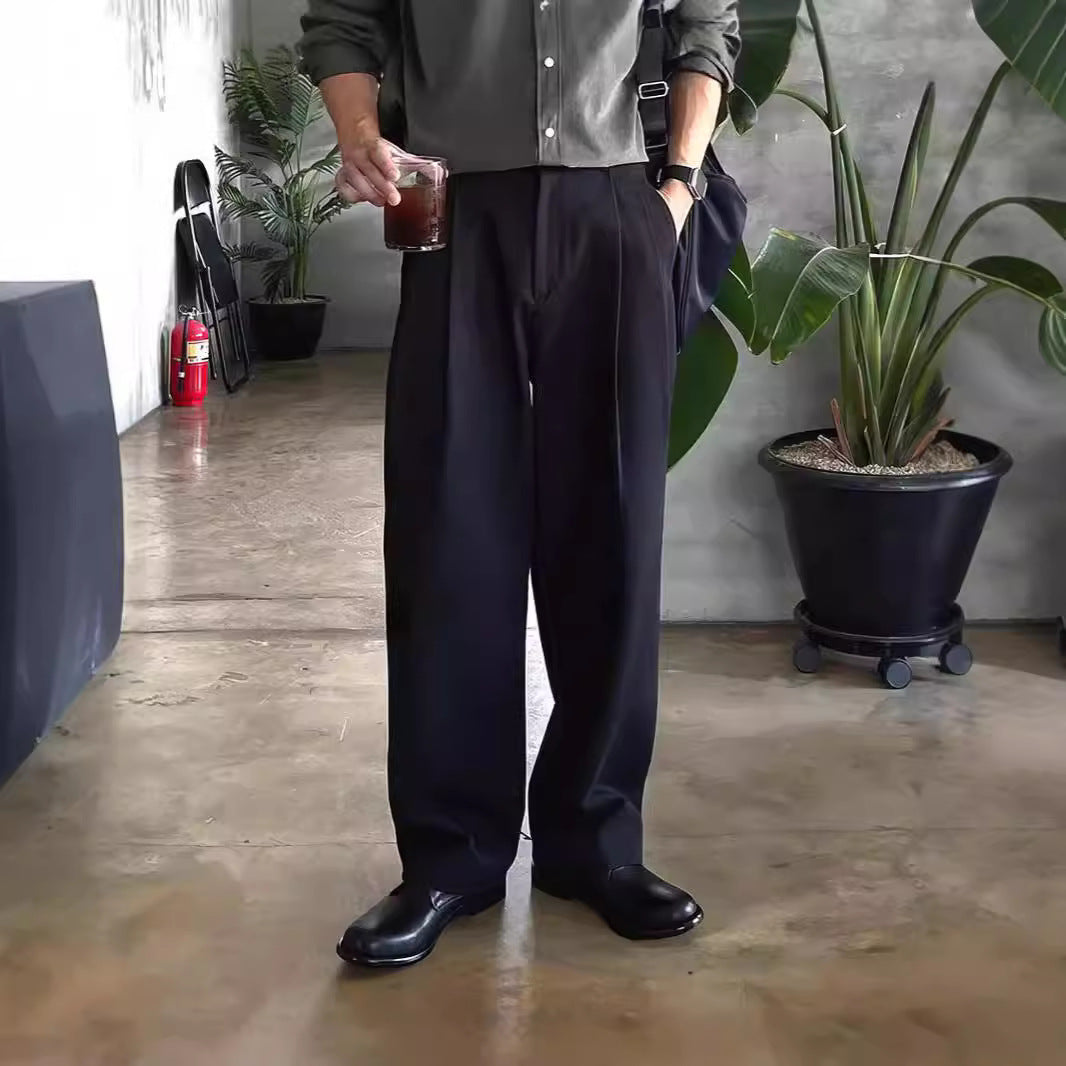 Mann in schwarzer Hose und Hemd hält Getränk, steht in modernem Raum mit Pflanzen. Stilvolle Herrenmode, lässiger Look, Indoor-Umgebung.