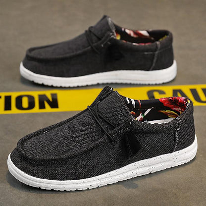 Dunkelgraue Freizeitschuhe mit weißer Sohle, floralem Innenfutter, auf Betonboden vor gelbem "Caution"-Band. Ideal für Herrenmode und Streetwear.