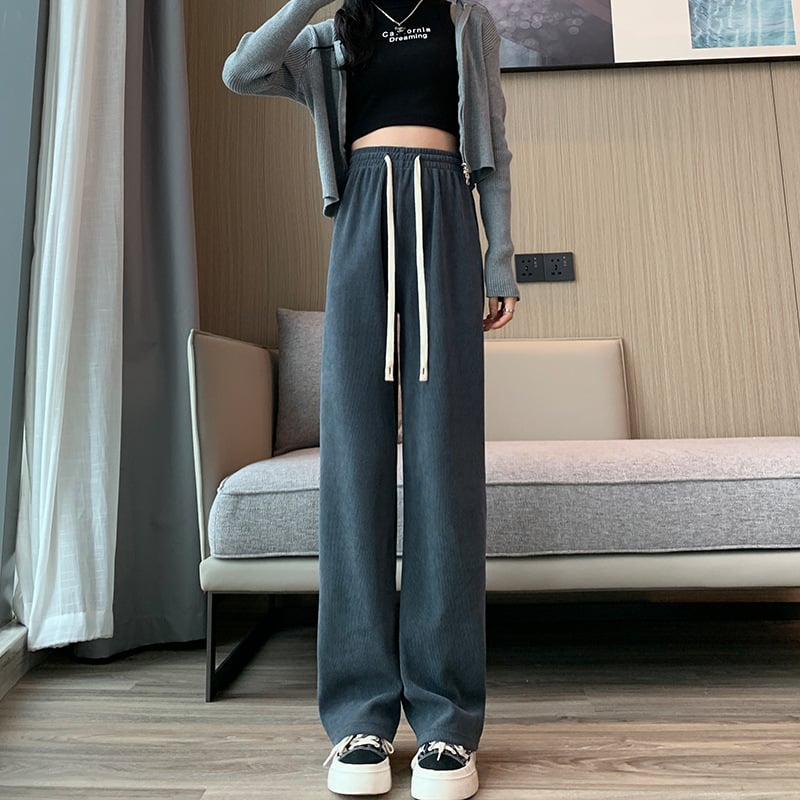 Frau in modischer Freizeitkleidung: Graue weite Hose, schwarzes Crop-Top, graue Strickjacke, Sneaker. Trendige Damenmode, lässiger Stil.