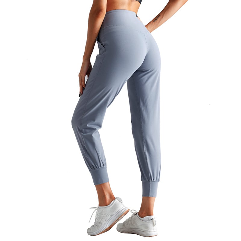 Frau in grauer Sporthose und weißen Sneakers, Rückansicht. Fitnessmode, bequeme Jogginghose, ideal für Sport und Freizeit.