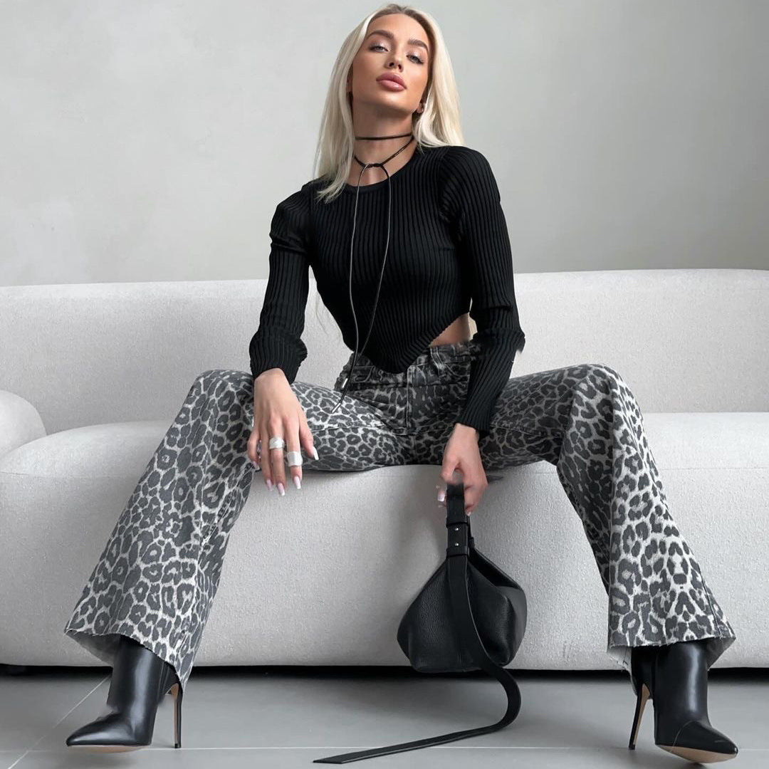 Blonde Frau in schwarzem Oberteil und Leopardenhose sitzt auf weißem Sofa, hält schwarze Tasche, trägt schwarze Stiefel. Modetrend, stilvoll, modern.