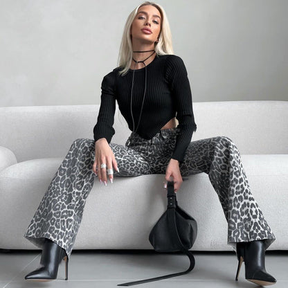 Blonde Frau in schwarzem Oberteil und Leopardenhose sitzt auf weißem Sofa, hält schwarze Tasche, trägt schwarze Stiefel. Modetrend, stilvoll, modern.