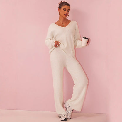 Frau in weißem Strickanzug mit Kaffeebecher, lässig an rosa Wand lehnend. Modetrend, gemütlicher Look, Damenmode, Freizeitkleidung.