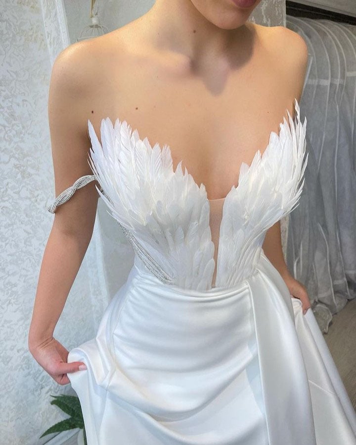 Brautkleid mit tiefem Ausschnitt und Federdetails, elegantes Design, weiße Seide, Hochzeitsmode, luxuriöses Brautkleid, moderne Brautmode.