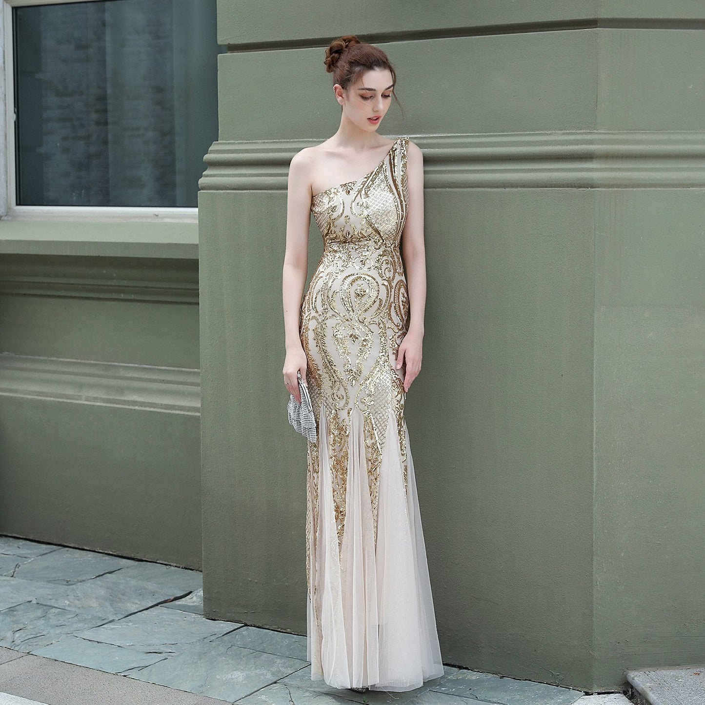 Elegantes Abendkleid in Gold mit Pailletten, bodenlang und schulterfrei, getragen von einer Frau vor einer grünen Wand. Perfekt für Gala oder Ball.