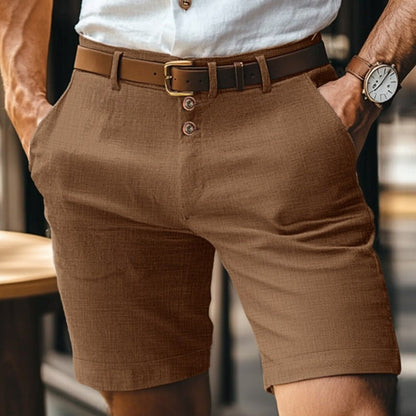 Mann in brauner Leinen-Shorts mit Gürtel und weißem Hemd, trägt Armbanduhr. Sommermode, Herrenbekleidung, stilvoll und lässig.