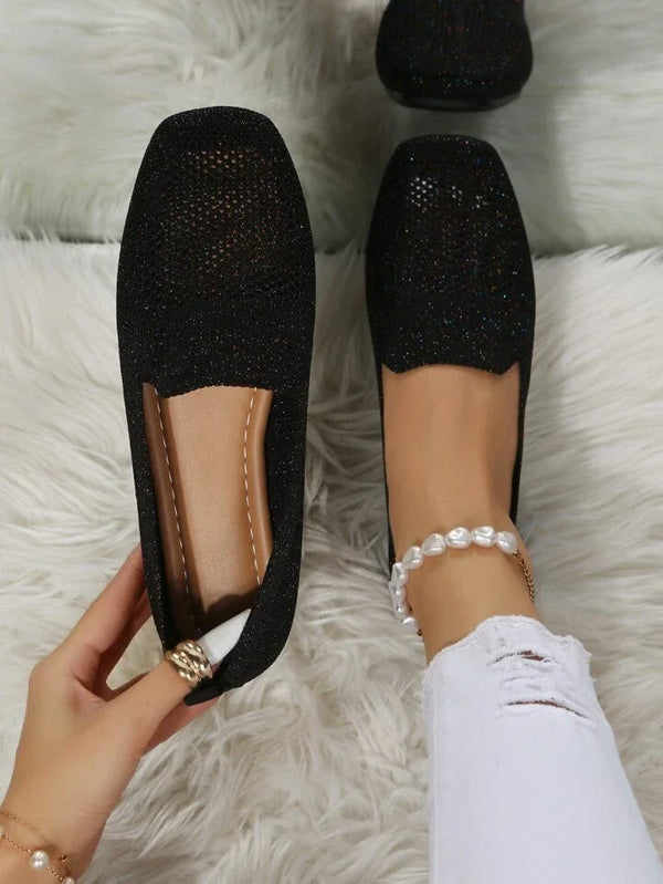 Schwarze, glitzernde Damen-Loafer auf weißem Teppich, getragen mit zerrissenen weißen Jeans und Perlenknöchelband. Elegante, modische Schuhe.