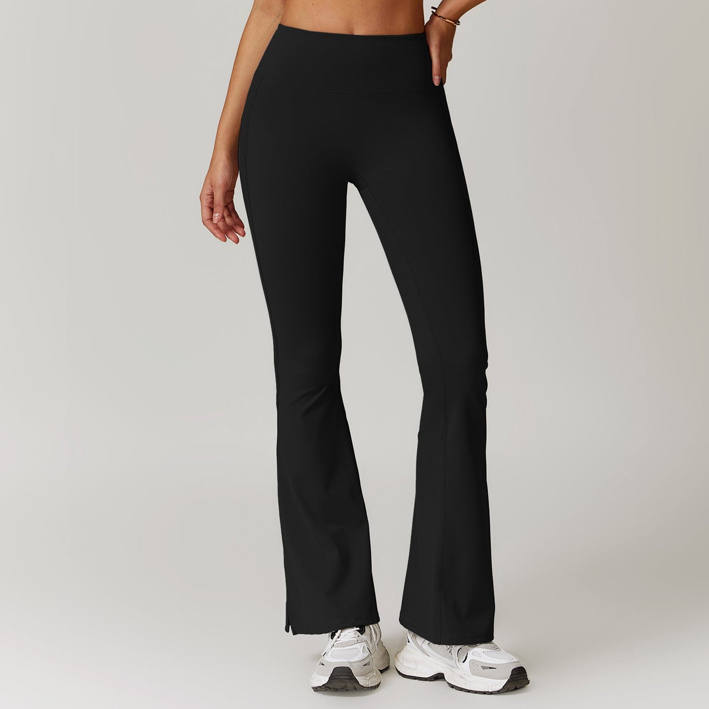 Frau trägt schwarze, ausgestellte Sportleggings und weiße Turnschuhe. Fitnessmode, bequeme Sportbekleidung, trendige Damenleggings.
