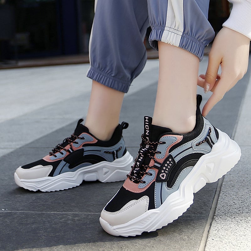Damen-Sneaker in Schwarz, Rosa und Grau mit dicker Sohle und Schnürung, getragen von Person in blauer Hose. Trendige Sportschuhe für Freizeit.