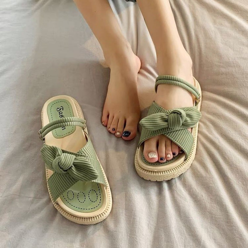 Grüne Sandalen mit Schleifen-Design auf Bett, getragen von einer Person. Modische Sommerschuhe, bequem und stilvoll für Damen.