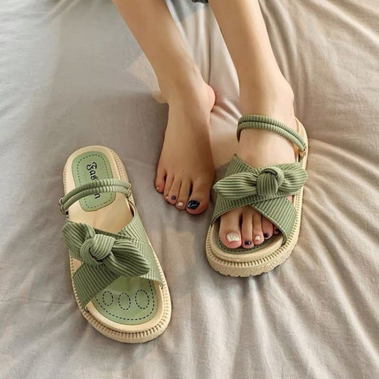 Grüne Sandalen mit Schleifen-Design auf Bett, getragen von einer Person. Modische Sommerschuhe, bequem und stilvoll für Damen.