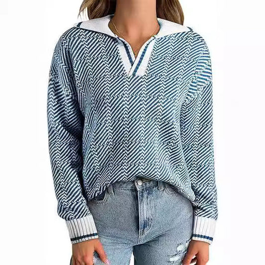 Frau trägt blauen Strickpullover mit Zickzackmuster und weißen Details, kombiniert mit hellblauen Jeans. Modetrend, Damenmode, Herbstoutfit.