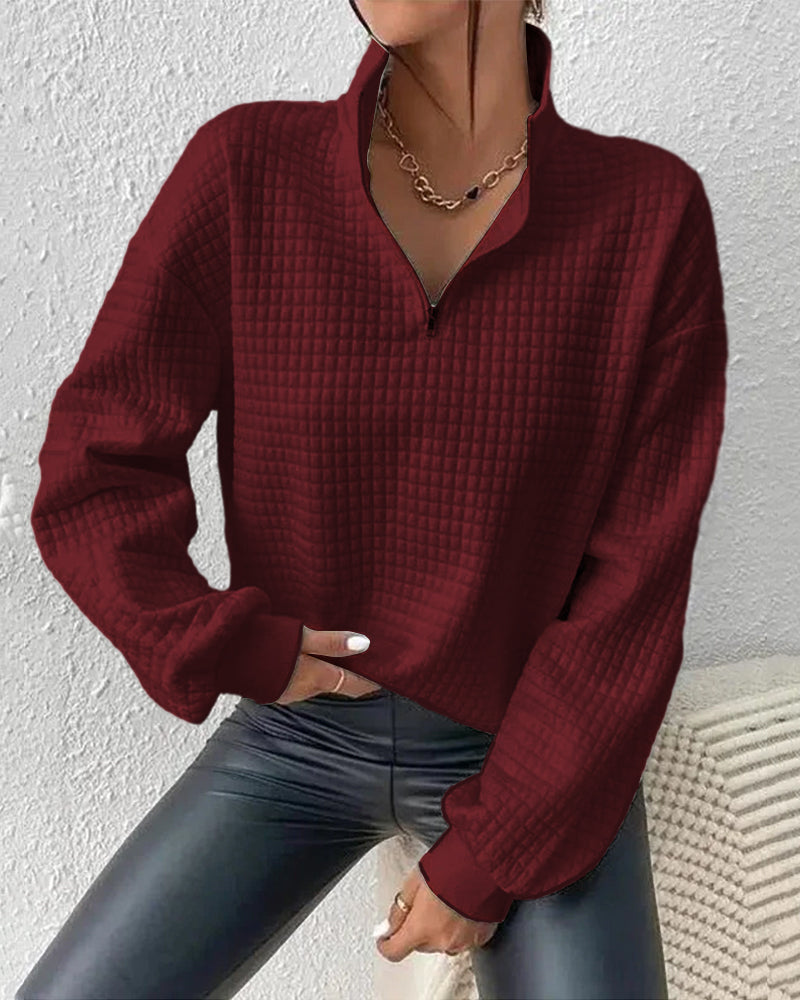 Frau trägt bordeauxroten Pullover mit Reißverschluss und Kettenhalskette, kombiniert mit schwarzer Lederhose. Modetrend, Herbstmode, Damenbekleidung.