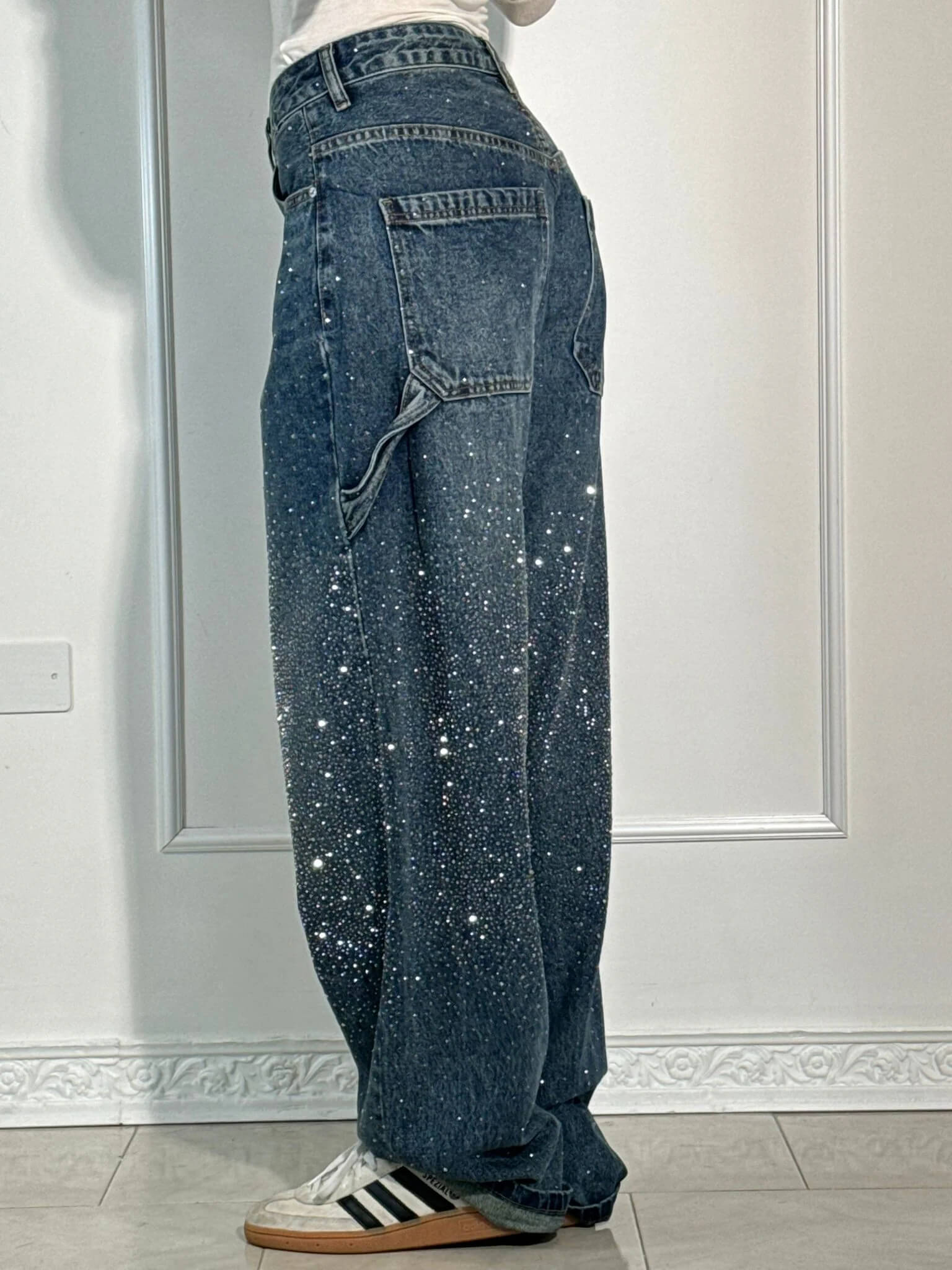 Damen-Jeans mit weitem Bein, verziert mit funkelnden Strasssteinen, kombiniert mit weißen Adidas-Sneakern. Trendige Mode für stilvolle Outfits.