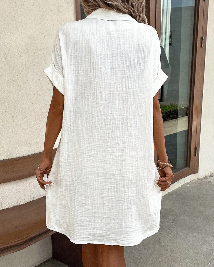 Frau in weißem Leinenkleid von hinten, lässiger Sommerlook, knielang, kurzärmlig, vor beigem Hintergrund, modisch und elegant.