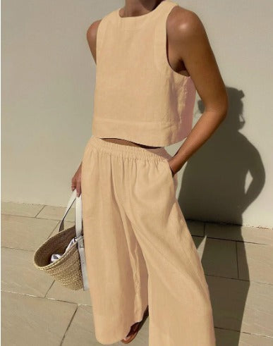 Frau in beigem Leinen-Zweiteiler mit ärmellosem Top und weiter Hose, hält eine Strohtasche. Sommermode, minimalistischer Stil, elegantes Outfit.