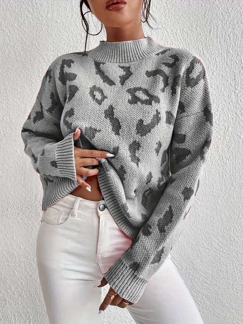 Frau in grauem Leopardenmuster-Pullover und weißen Jeans vor weißer Wand. Modetrend, Herbstmode, Damenbekleidung, stilvoller Look.