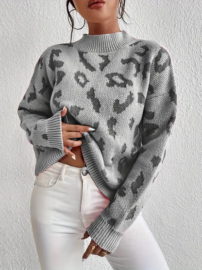Frau in grauem Leopardenmuster-Pullover und weißen Jeans vor weißer Wand. Modetrend, Herbstmode, Damenbekleidung, stilvoller Look.
