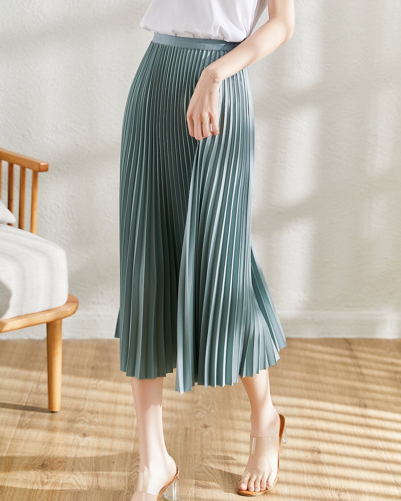 Frau trägt eleganten, blauen Plisseerock, kombiniert mit weißem Oberteil. Modetrend, Damenmode, stilvoller Look, Sommeroutfit, Plisseerock.