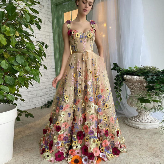 Frau in elegantem, blumengeschmücktem Abendkleid vor weißer Backsteinwand und Pflanzen. Romantisches Design, florale Mode, Ballkleid.