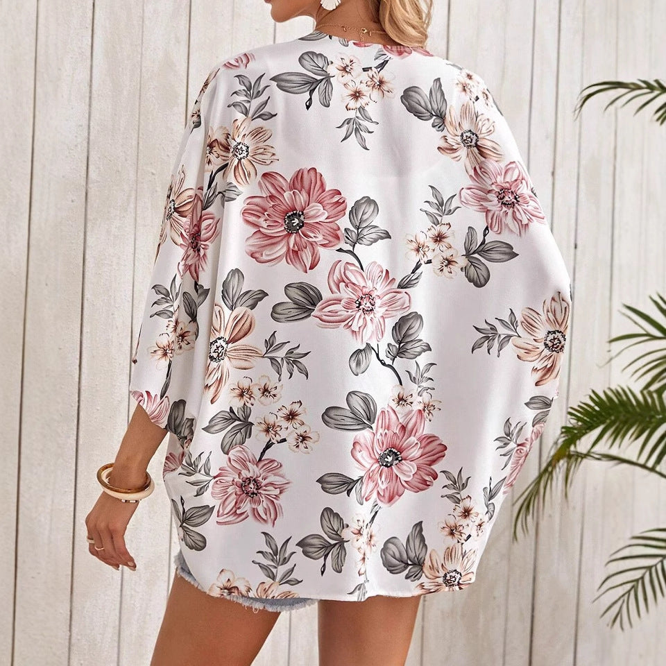 Frau in weißem, geblümtem Kimono vor Holzwand, Sommermode, florales Design, lässiger Stil, Rückansicht, tropische Pflanzen im Hintergrund.