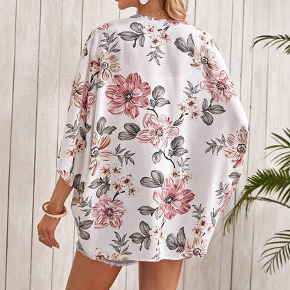Frau in weißem, geblümtem Kimono vor Holzwand, Sommermode, florales Design, lässiger Stil, Rückansicht, tropische Pflanzen im Hintergrund.