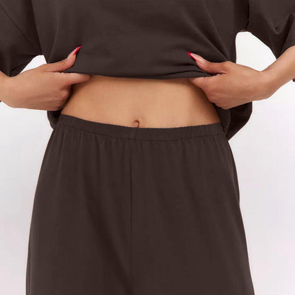 Frau zeigt Bauch in braunem Outfit, hebt Oberteil an. Mode, Bauch, Kleidung, Freizeitlook, Damenmode, braunes Outfit, lässiger Stil.