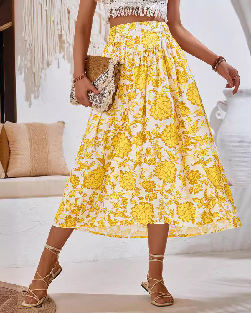 Frau in gelbem Blumenrock und weißem Top, hält eine Strohtasche. Sommermode, Boho-Stil, elegantes Outfit, Sandalen, Innenraum mit Sofa.