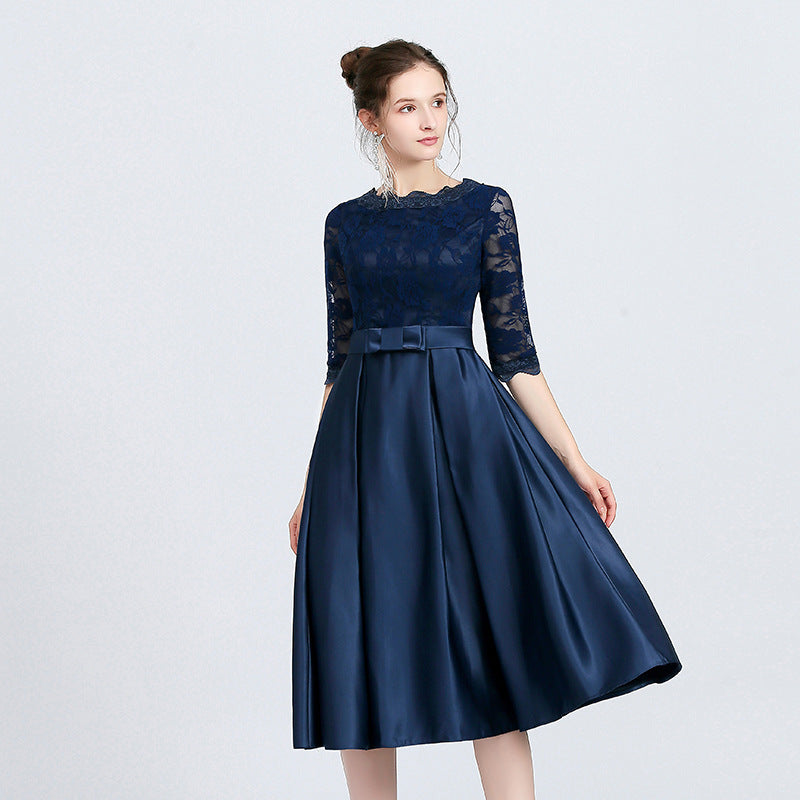 Frau in elegantem, dunkelblauem Abendkleid mit Spitzenoberteil und halblangen Ärmeln, posiert vor hellem Hintergrund. Perfekt für formelle Anlässe.