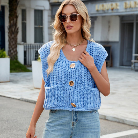 Frau mit blauer Strickweste und Sonnenbrille, steht auf einer Straße. Modetrend, lässiger Stil, Sommermode, Damenbekleidung, urbane Kulisse.