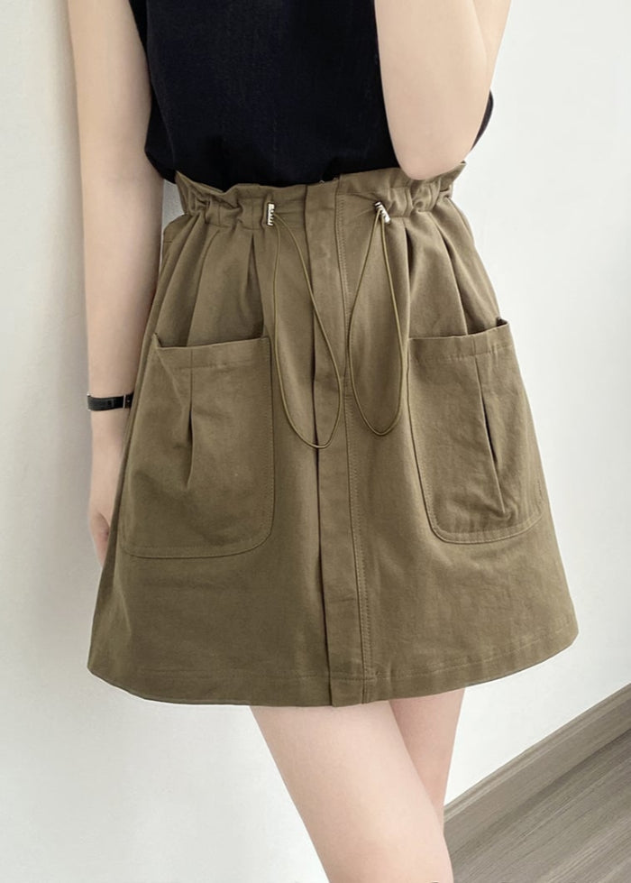 Frau trägt olivgrünen Rock mit Taschen und Kordelzug, kombiniert mit schwarzem Oberteil. Modetrend, lässiger Stil, Damenmode, Sommeroutfit.