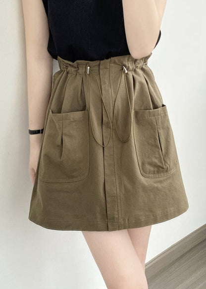 Frau trägt olivgrünen Rock mit Taschen und Kordelzug, kombiniert mit schwarzem Oberteil. Modetrend, lässiger Stil, Damenmode, Sommeroutfit.