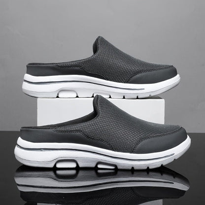 Graue Herren-Sneaker-Slipper mit weißer Sohle, atmungsaktivem Mesh-Obermaterial, auf weißem Podest vor grauem Hintergrund. Bequeme Freizeitschuhe.