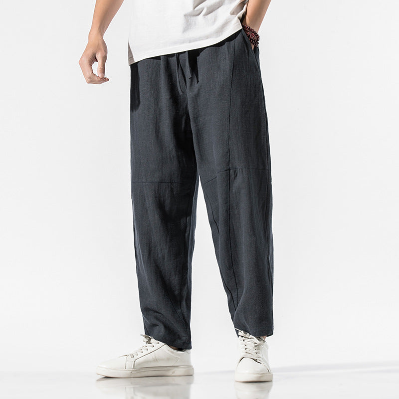 Mann in grauer Leinenhose und weißen Sneakers vor weißem Hintergrund. Bequeme, lässige Mode für Herren.