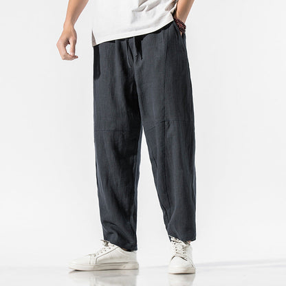 Mann in grauer Leinenhose und weißen Sneakers vor weißem Hintergrund. Bequeme, lässige Mode für Herren.