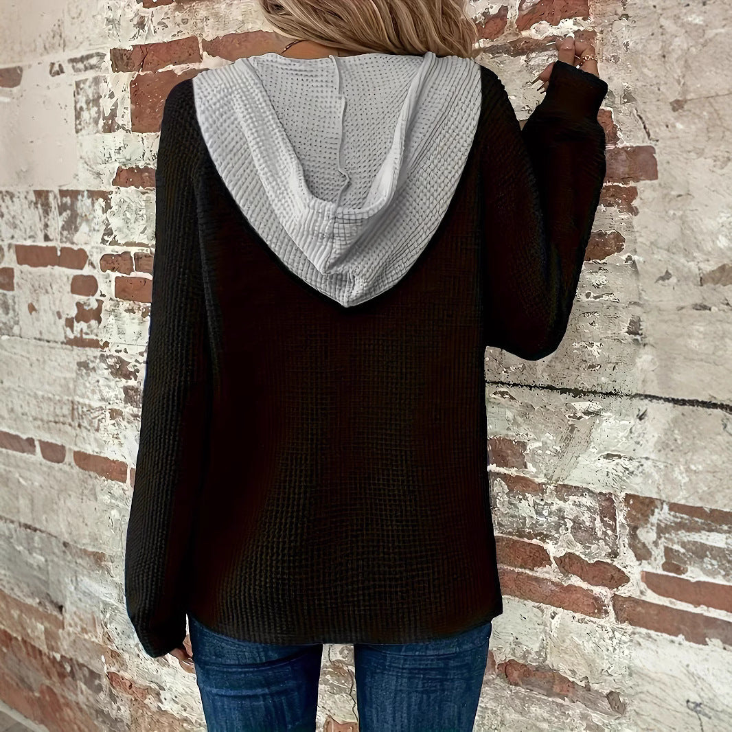 Frau in schwarzem Kapuzenpullover und blauer Jeans vor einer Backsteinmauer. Modetrend, lässiger Stil, Herbstmode.