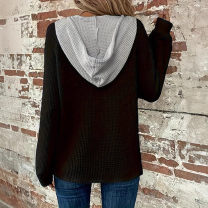 Frau in schwarzem Kapuzenpullover und blauer Jeans vor einer Backsteinmauer. Modetrend, lässiger Stil, Herbstmode.