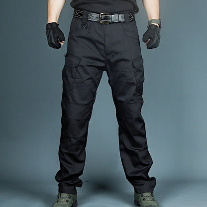 Schwarze taktische Hose mit mehreren Taschen, getragen von Person in schwarzem Outfit und Handschuhen, ideal für Outdoor-Aktivitäten und Sicherheit.
