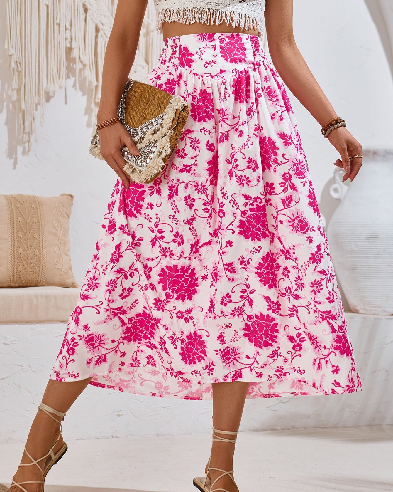 Frau in weißem und pinkem Blumenrock, hält eine beige Clutch. Sommermode, Boho-Stil, modisches Outfit, feminine Kleidung, Freizeitlook.