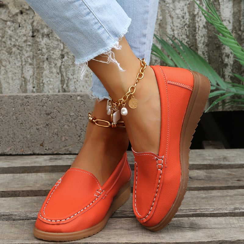Orange Damen-Loafer aus Leder, kombiniert mit zerrissenen Jeans und goldener Fußkette. Modischer, bequemer Freizeitschuh für den Alltag.