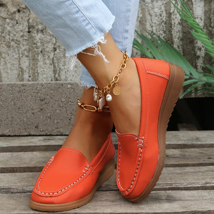 Orange Damen-Loafer aus Leder, kombiniert mit zerrissenen Jeans und goldener Fußkette. Modischer, bequemer Freizeitschuh für den Alltag.