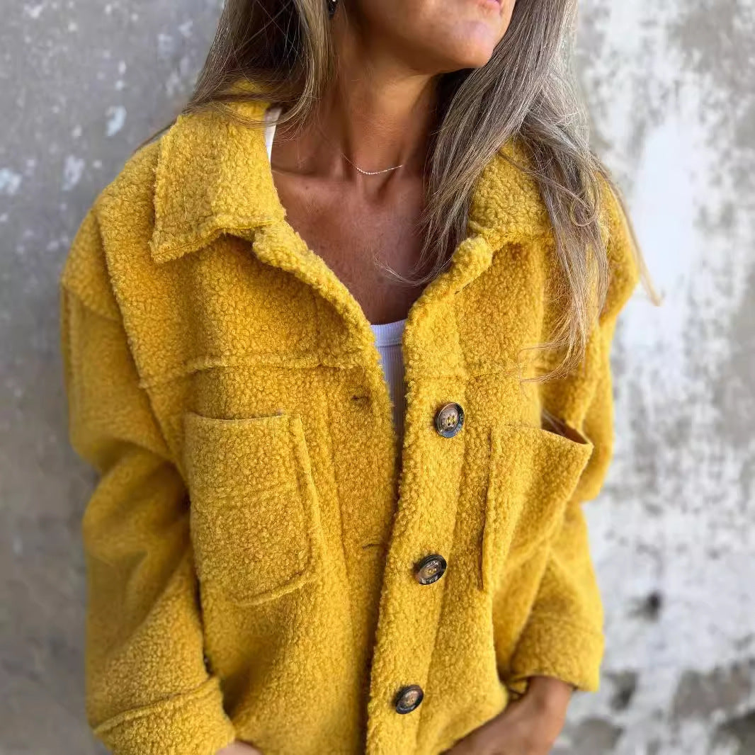 Frau in gelber Teddyjacke mit Knöpfen vor Betonwand. Modetrend, Herbstmode, Damenjacke, kuscheliger Look, Streetstyle.