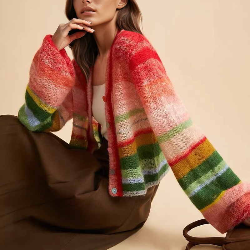 Frau trägt bunte, gestreifte Strickjacke mit Rot-, Grün- und Gelbtönen, kombiniert mit brauner Hose. Modetrend Herbst 2023, gemütlicher Look.