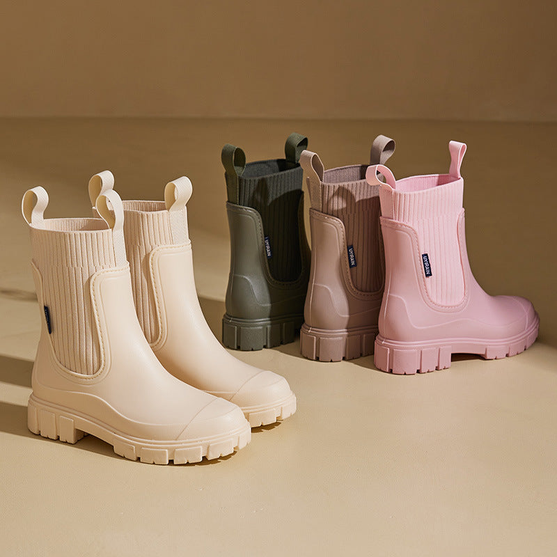 Drei Paar modische Gummistiefel in Beige, Olivgrün und Rosa auf beigem Hintergrund. Trendige Damenstiefel, wasserdicht, ideal für Herbst und Winter.