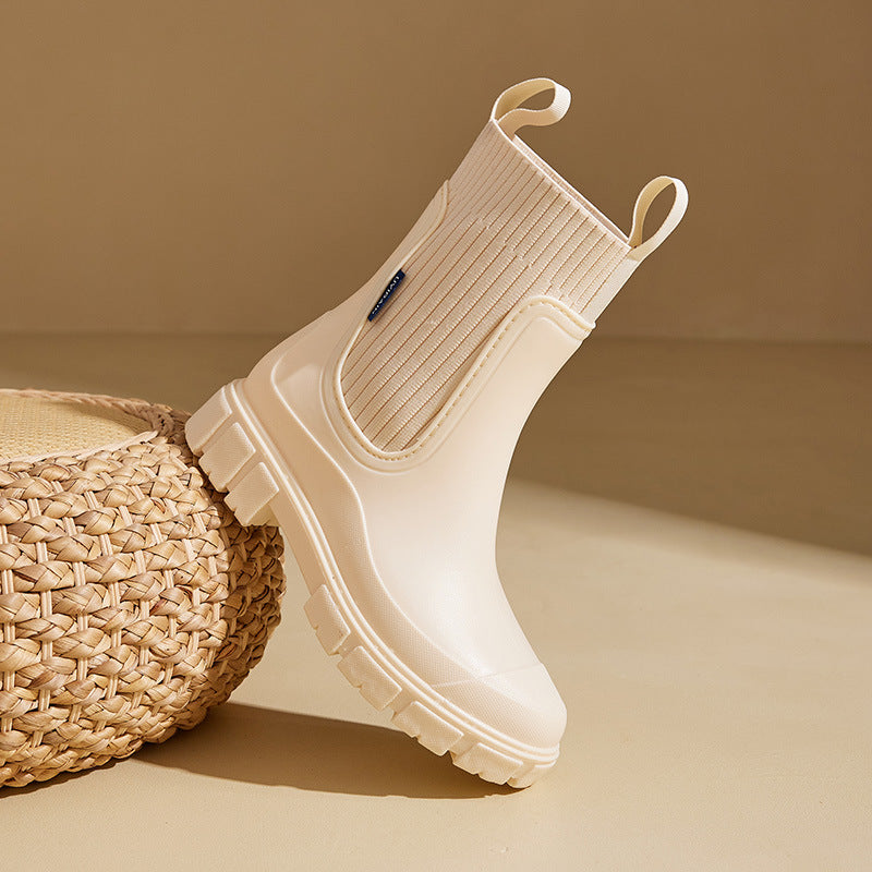 Beige Gummistiefel mit dicker Sohle und seitlichen Schlaufen auf beigem Hintergrund. Modische Regenstiefel, wasserdicht, rutschfest.