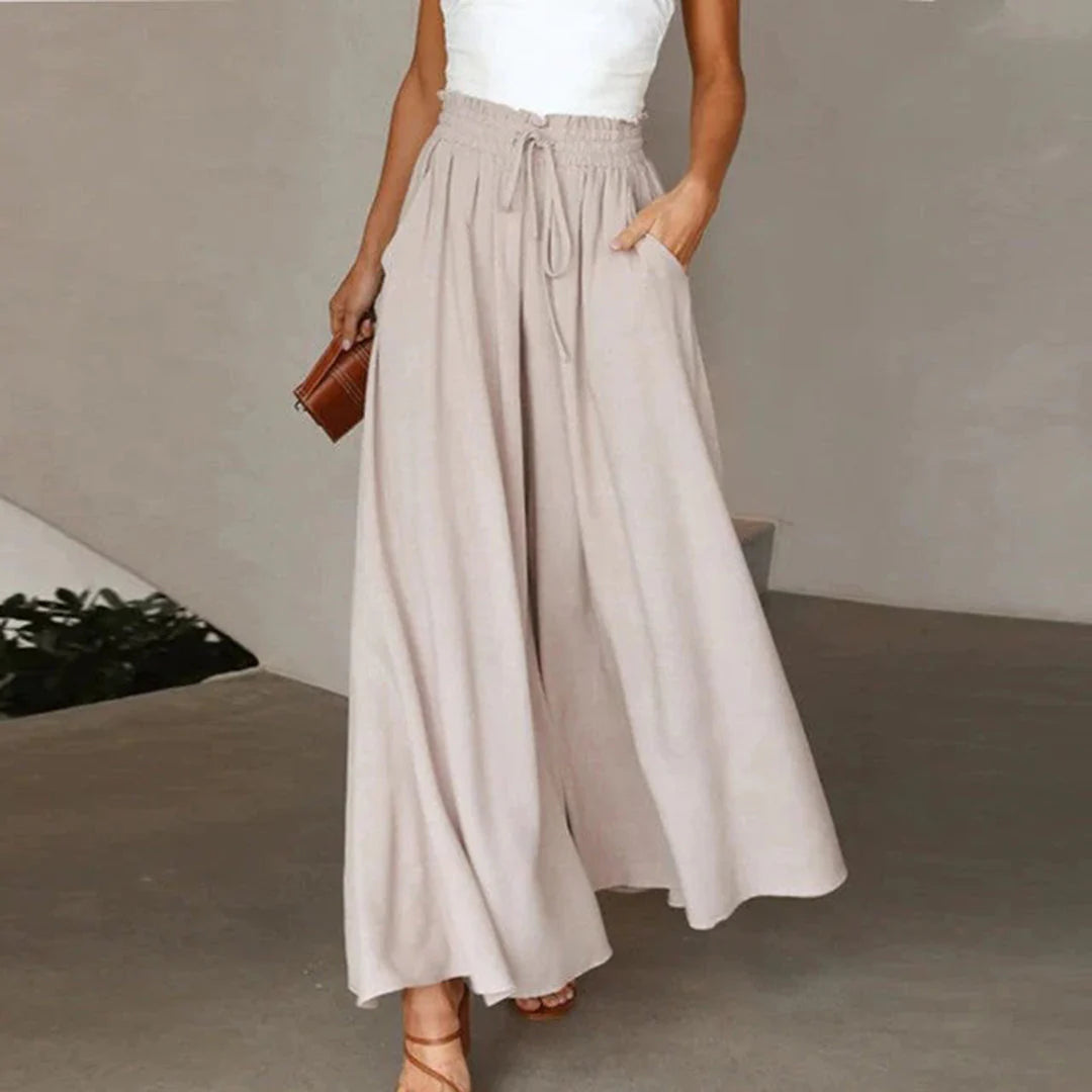 Frau in beiger, weiter Palazzo-Hose und weißem Top, hält eine kleine braune Tasche. Modetrend, Sommeroutfit, elegante Damenbekleidung.