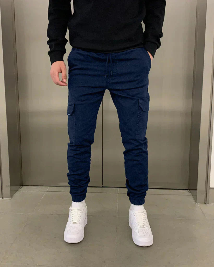Mann in blauer Jogginghose und weißen Sneakers vor Aufzugstür. Bequeme Freizeitmode, Herrenbekleidung, urbane Streetwear.