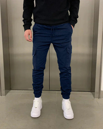Mann in blauer Jogginghose und weißen Sneakers vor Aufzugstür. Bequeme Freizeitmode, Herrenbekleidung, urbane Streetwear.