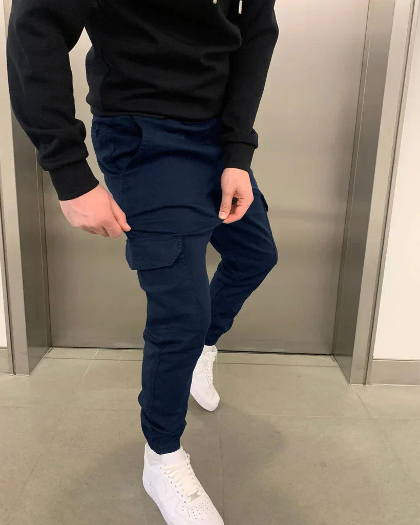 Mann in dunkelblauer Cargohose und weißen Sneakers vor einem Aufzug. Modetrend, Herrenbekleidung, lässiger Stil.
