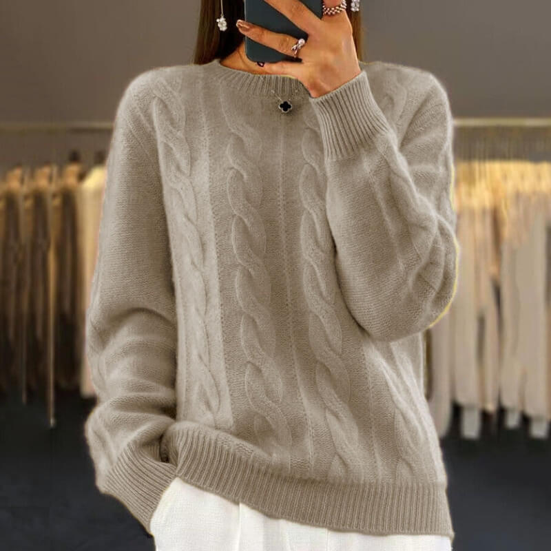 Frau in beigem Zopfmuster-Pullover, hält Smartphone, vor Kleiderständer. Modetrend, Herbstmode, Strickpullover, Damenbekleidung.